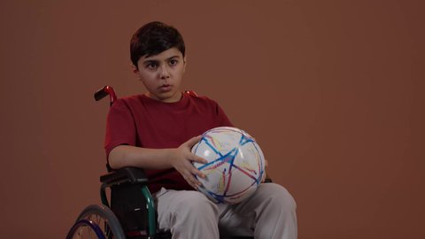 ايماءات الفرح والحماس , المباريات والالعاب الرياضية, التفاعل والاندماج بمشاهدة الفريق المفضل, بورتريه لولد عربي سعودي خليجي يجاس على كرسي متحرك يمسك بيده كرة قدم, الشغف بالانشطة الترفيهية