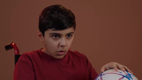 التفاعل والاندماج بمشاهدة الفريق المفضل, المباريات والالعاب الرياضية, ايماءات الفرح والحماس , بورتريه لولد عربي سعودي خليجي يجاس على كرسي متحرك يمسك بيده كرة قدم, الشغف بالانشطة الترفيهية