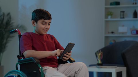 تصفح الإنترنت والمحادثات، التواصل مع الأصدقاء،استخدام الأطفال للتكنولوجيا الحديثة, ولد عربي خليجي سعودي يرتدي الزي الكاجوال يجلس على كرسي متحرك ويستخدم الجوال، إجراء مكالمة فيديو