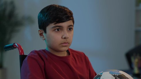 ايماءات الفرح والحماس , التفاعل والاندماج بمشاهدة الفريق المفضل, المباريات والالعاب الرياضية, بورتريه لولد عربي سعودي خليجي يجاس على كرسي متحرك يمسك بيده كرة قدم, الشغف بالانشطة الترفيهية