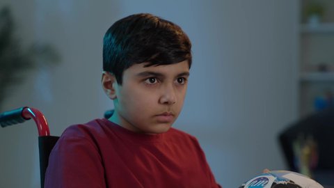 المباريات والالعاب الرياضية, التفاعل والاندماج بمشاهدة الفريق المفضل,ايماءات الفرح والحماس , بورتريه لولد عربي سعودي خليجي يجاس على كرسي متحرك يمسك بيده كرة قدم, الشغف بالانشطة الترفيهية