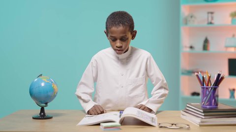 Reviewing lessons diligently and diligently to achieve success and excellence, focusing on solving and writing assignments, returning to school, a Saudi Arabian Gulf student wearing traditional clothing sitting at a desk
