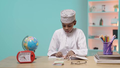 Hard work and diligence to achieve success and excellence, back to school, an Arab Gulf Omani student wearing a dishdasha and a kummah sitting in his seat reading, blue background