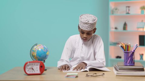 استغلال الوقت في الدراسة والمذاكرة، العودة إلى المدارس، طالب عربي خليجي عماني يرتدي الدشداشة والكمة يجلس في مقعده يقوم بالقراءة, خلفية زرقاء