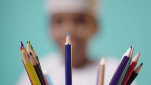 Close-up of a set of colored wooden pencils, blurry background of an Omani Gulf Arab boy choosing a colored pencil, education in schools in the Sultanate of Oman, development and growth of hobbies