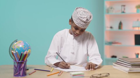 تطوير وتنمية الهوايات, إيماءات الاندماج والتركيز في الأنشطة الفنية، تلميذ عربي خليجي عماني يرتدي الدشداشه والكمه يجلس في مقعده يقوم بالتلوين