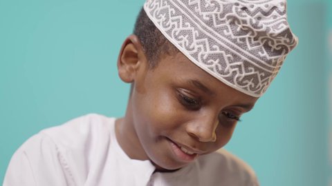 علامات الاندماج والسعادة والسرور, موسم العودة للمدارس، إنجاز الواجبات اليومية، تلميذ عربي خليجي عماني يرتدي الدشداشه والكمه مندمج في الدراسة, خلفية زرقاء