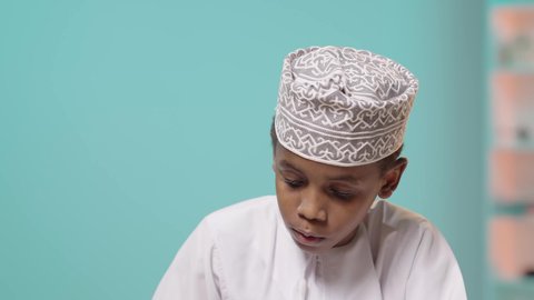 ثقافة التعلم الذاتي, الاستمتاع بقراءة الكتب، موسم العودة للمدارس، إنجاز الواجبات اليومية، بورتريه لتلميذ عربي خليجي عماني يرتدي الدشداشه والكمة مندمج في القراءة, خلفية زرقاء