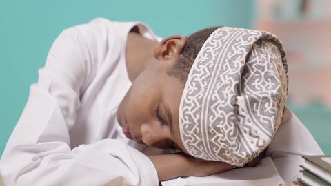 الشعور بالتعب والنعاس من الدراسة، متابعة المناهج الدراسية, طالب عربي خليجي عماني يرتدي الدشداشة والكمة نائم على طاولة الدراسة، دخول وقت النوم, سلبيات التعلم عن بعد, خلفية زرقاء
