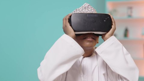 اتباع طرق تعليمية جديدة، مدارس وأكاديميات متطوره، بورتريه لتلميذ عربي خليجي عماني يرتدي الدشداشة والكمة يضع نظارات الواقع الافتراضي، جمع التعلم مع الترفيه، إستخدام التقنيه والتكنولوجيا الحديثه, خلفية زرقاء