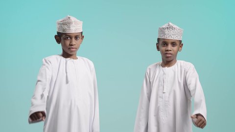 الاشارة بعلامة اللايك، إيماءات وجه ويدين تدل على الإعجاب والرضا, بورتريه لولدين عربيين خليجيين عمانيين يرتديان الدشداشة و الكمة يقومان برفع أصبع الإبهام الى أعلى, خلفية زرقاء