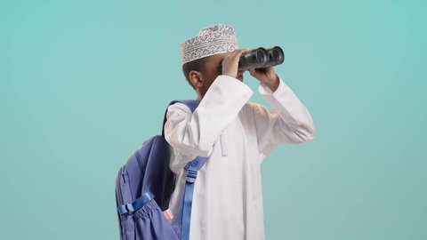 التخطيط المستقبلي للأهداف والطموحات، حب الاستكشاف والمغامرة، بورتريه لولد عربي خليجي عماني يرتدي الدشداشة والكمة يمسك منظار ثنائي العينين ينظر إلى الكاميرا بإيماءات السرور، التفكير والتطلع إلى المستقبل, خلفية زرقاء