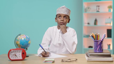 التركيز في حل وكتابة الواجب، مراجعة الدرس بجد واجتهاد للوصول إلى النجاح والتفوق، العودة إلى المدارس، طالب عربي خليجي عماني يرتدي الدشداشة والكمة يقوم بالتفكير في حل مسألة, خلفية زرقاء