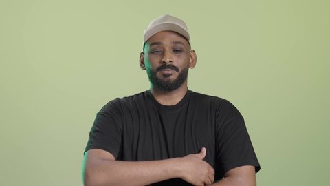 الوقوف بيدين متقاطعتين يإيماءات الثقة بالنفس، عمليات إيصال الطلبات إلى الزبائن بسهولة، بورتريه لمندوب عربي خليجي سعودي يرتدي الزي الكاجوال و قبعة بيج يقف باستقامة و ينظر الي الكاميرا و هو يبتسم, خلفية خضراء