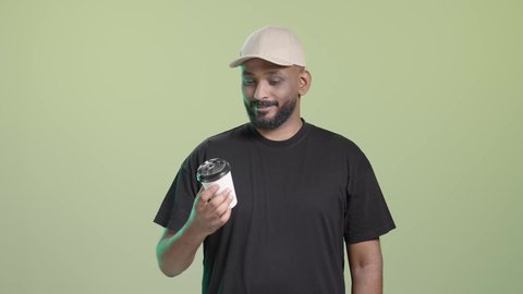 ضمان سلامة الطرود المرسلة، تسليم الطلبات والبضائع بأمان وسرعة، توصيل المشروبات الساخنة، ، بورتريه لمندوب عربي خليجي سعودي يرتدي الزي الكاجوال و قبعة بيج يحمل كوب ساخن و يسلمه بابتسامة, خلفية خضراء