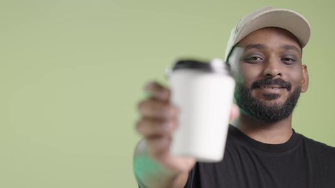 تسليم الطلبات والبضائع بأمان وسرعة، توصيل المشروبات الساخنة، بورتريه لمندوب عربي خليجي سعودي يرتدي الزي الكاجوال و قبعة بيج يحمل كوب ساخن و يسلمه بابتسامة, خلفية خضراء