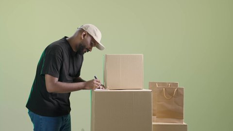 التأكد من وجود البضائع وتوافرها، تسليم الطلبات في الموعد المحدد، التسوق الالكتروني والتطور, بورتريه لرجل عربي خليجي سعودي يرتدي الزي الكاجوال و قبعة بيج يضع صندوق كرتوني, مراجعة الطلبات و تدوين الملاحظات, خلفية خضراء