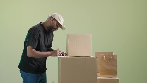 التوقيع على أوراق و مستندات استلام وتسليم الطرود، بورتريه لمندوب عربي خليجي سعودي يرتدي الزي الكاجوال و قبعة بيج يقوم بتدوين و مراجعة الطلب, خلفية خضراء