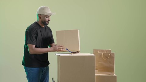 التسوق الالكتروني والتطور, بورتريه لرجل عربي خليجي سعودي  يرتدي الزي الكاجوال و قبعة بيج يعمل في مخزن توصيل الطلبات والبضائع للزبائن, مراجعة الطلبات و تدوين الملاحظات, خلفية خضراء