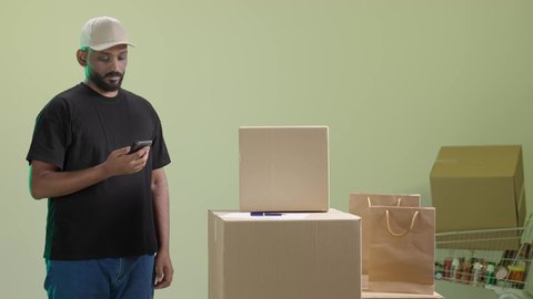 خدمة التوصيل السريع في السعودية، التواصل الفعال مع العملاء، مفهوم الآمان في نقل طلبيات الاونلاين، بورتريه لمندوب عربي خليجي سعودي مبتسم يرتدي الزي الكاجوال و قبعة بيج يحمل هاتف محمول و يقوم بعرض الشاشة, خلفية خضراء