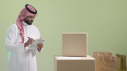 مفهوم التسوق الالكتروني, عملية شحن وتوصيل موثوقة, بورتريه لمندوب عربي خليجي سعودي يرتدي الزي التقليدي والشماغ يقوم بتدوين و مراجعة الطلب, خلفية خضراء