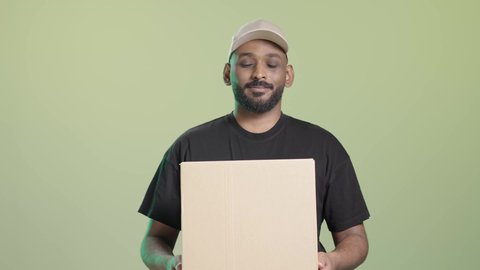 ايماءات السعادة و السرور, عملية شحن وتوصيل موثوقة, بورتريه لمندوب عربي خليجي سعودي يرتدي الزي الكاجوال و قبعة بيج يحمل صندوق كرتوني و يسلمه بابتسامة, خلفية خضراء