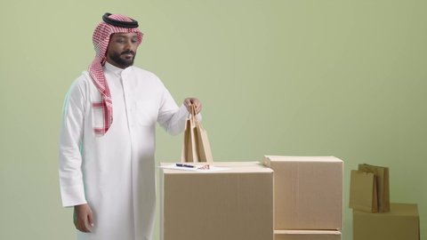 كتابة وتسجيل البيانات والملاحظات، مفهوم التسوق الالكتروني, الطلبات الاونلاين والتسوق الذكي, عملية شحن و توصيل موثوقه, بورتريه لمندوب عربي خليجي سعودي يرتدي الزي التقليدي والشماغ يقوم بتدوين الطلب, خلفية خضراء