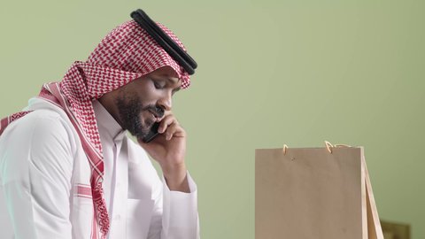 ادارة عملية الشحن والتوصيل, بورتريه لرجل عربي خليجي سعودي يرتدي الزي التقليدي والشماغ يقوم بالتواصل مع العميل من خلال الجوال و تدوين الطلب, خلفية خضراء