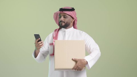 إنجاز الأعمال باستعمال الهاتف المحمول، استخدام الأجهزة التقنية الحديثة، بورتريه لرجل عربي خليجي سعودي مبتسم يرتدي الزي التقليدي والشماغ يحمل هاتف محمول و صندوق كرتوني, عملية شحن و توصيل موثوقة, خلفية خضراء