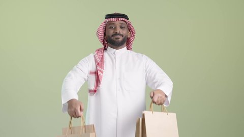 توصيل الطلبات في الوقت المحدد و بشكل سليم، التسوق و طلب المنتجات عبر الإنترنت، بورتريه لمندوب عربي خليجي سعودي يرتدي الزي التقليدي و الشماغ يحمل أكياس و يسلمها بابتسامة, ايماءات السعادة و السرور, خلفية خضراء