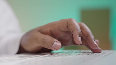 Tapping on laptop, completing work tasks remotely, managing and organizing business affairs via tablet, close-up portrait of hand of Saudi Arabian Gulf man wearing traditional dress typing on keyboard, Blurry background of cardboard boxes