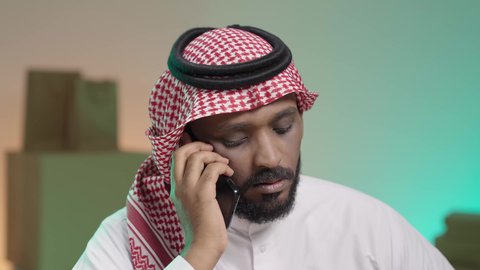 الرد على الاتصالات والاستفسارات, التواصل الفعال مع العملاء, بورتريه لرجل عربي خليجي سعودي يرتدي الزي التقليدي والشماغ يقوم بالتحدث مع العميل من خلال الجوال, خلفية ملونة
