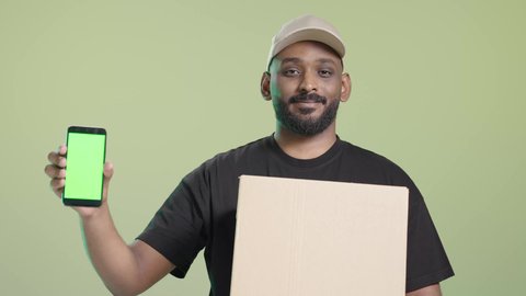 خدمة العملاء و عملية توصيل الطلبات للزبائن، الشحن ذات الجودة العالية، الاستفادة من التكنولوجيا الحديثة بتسهيل العمل، بورتريه لمندوب عربي خليجي سعودي مبتسم يرتدي الزي الكاجوال و قبعه بيج يحمل هاتف محمول و صندوق كرتوني, خلفية خضراء