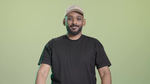 التسوق وطلب المنتجات عبر الإنترنت، توصيل الطلبات في الوقت المحدد وبشكل سليم،  بورتريه لمندوب عربي خليجي سعودي يرتدي الزي الكاجوال و قبعة بيج يحمل أكياس ويسلمها بابتسامة,  ايماءات السعادة و السرور, خلفية خضراء