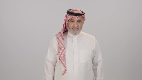 The concept of concern for outward appearance, masculinity and elegance, a portrait of an elderly Saudi Arabian Gulf Arab man wearing a shemagh and traditional dress, standing straight with his hands crossed, looking at the camera with expressions of happiness and pleasure