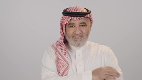 ايماءات الثقة بالنفس، مفهوم الاهتمام بالمظهر الخارجي و الرجولة والأناقه، بورتريه لرجل كبير بالسن عربي خليجي سعودي يرتدي الشماغ والزي التقليدي يقف باستقامة بايدي متقاطعه, النظر إلى الكاميرا بتعابير السعادة والسرور