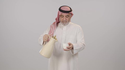 ملامح الأصالة وروح التواصل الاجتماعي,  بورتريه لرجل مسن عربي خليجي سعودي مبتسم يرتدي الثوب التقليدي و الشماغ يحمل دلة تقليدية و يسكب القهوة في فنجان صغير, تأدية واجب الضيافة