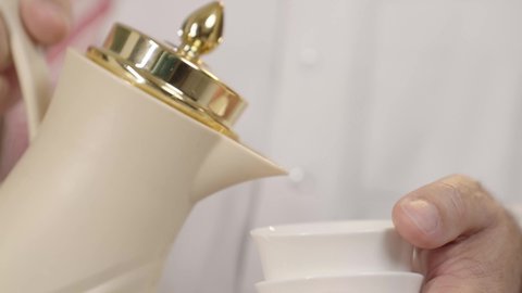 لقطة قريبة تبرز تفاصيل الضيافة العربية، يد رجل عربي خليجي سعودي مسن يحمل دلة تقليدية و يسكب القهوة في فنجان صغير، عادات استقبال الضيوف بروح الود والكرم