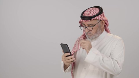 التواصل والدردشة مع الأهل والأصدقاء عبر تطبيقات الجوال, بورتريه لرجل مسن عربي خليجي سعودي يرتدي الثوب التقليدي و الشماغ يضع النظارة الطبية, تصفح مواقع التواصل الاجتماعي