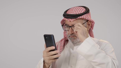تصفح مواقع التواصل الاجتماعي, التواصل والدردشة مع الأهل والأصدقاء عبر تطبيقات الجوال, بورتريه لرجل مسن عربي خليجي سعودي يرتدي الثوب التقليدي و الشماغ  يضع النظارة الطبية