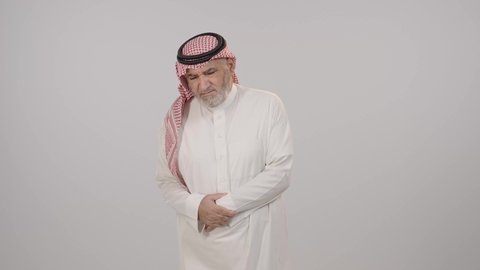 ضرورة أخذ الدواء للتعافي من المرض، إمساك البطن والشعور بآلام المغص، بورتريه لرجل مسن عربي خليجي سعودي يرتدي الثوب التقليدي و الشماغ يضع يديه على معدته بإيماءات الاضطراب والانزعاج، أهمية زيارة الطبيب والحصول على قسط من الراحة