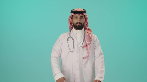 الاستعداد لتقديم الخدمات للمرضى بكل كفاءة، مفهوم الطب والرعاية الصحية، بورتريه لطبيب عربي خليجي سعودي مبتسم يرتدي الثوب التقليدي والشماغ مع المعطف الأبيض يضع سماعة الفحص ينظر إلى الكاميرا بتعابير السعادة والسرور، الوقوف باستقامة بايماءات ايدي متقاطعة, خلفية زرقاء