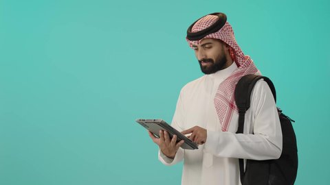 متابعة الدرجات من خلال التابلت, تطوير المناهج التعليمية في السعودية، الاجتهاد وتحضير الدروس, بورتريه لرجل عربي خليجي سعودي مبتسم يرتدي الثوب الأبيض التقليدي و الشماغ و حقيبة الظهر يحمل بيده الحاسوب اللوحي, خلفية زرقاء