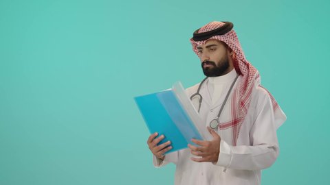 التقارير والتحاليل الطبية، العمل في القطاع الصحي في المملكة العربية السعودية، تقديم الرعاية والخدمات الصحية، بورتريه لطبيب عربي خليجي سعودي يرتدي الثوب التقليدي و الشماغ مع المعطف الأبيض يضع سماعة الفحص و يقوم بقراءة ملفات و أوراق المرضى, خلفية زرقاء