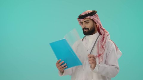 قراءة ملفات و أوراق المرضى، التقارير والتحاليل الطبية، العمل في القطاع الصحي في المملكة العربية السعودية، تقديم الرعاية والخدمات الصحية، بورتريه لطبيب عربي خليجي سعودي يرتدي الثوب التقليدي و الشماغ مع المعطف الأبيض يضع سماعة الفحص, خلفية زرقاء