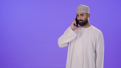 الدردشة مع الأهل والأصدقاء، تبادل الاخبار عبرمكالمة هاتفيه، بورتريه لرجل عربي خليجي عماني يرتدي الدشداشة والكمه يقوم بالتواصل مع الأقارب، تعابير الفرح والسرور، خلفية بنفسجية