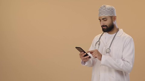 تقديم الخدمات والرعاية الصحية عبر الإنترنت، بورتريه لطبيب عربي خليجي عماني يرتدي الدشداشة و الكمة و  المعطف الطبي و السماعه يقوم باستخدام الهاتف المحمول، استخدام الأجهزة التقنية الحديثة ودمج التكنولوجيا مع الطب، التطبيقات والبرامج الصحية، خلفية بنية