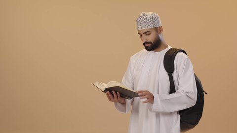 قراءة الكتب الجامعية، مراجعة الدروس اليومية، بورتريه طالب جامعي عربي خليجي عماني يرتدي الدشداشة و الكمه يضع الحقيبة على ظهرة يحمل بيده كتاب جامعي، التعليم الجامعي في سلطنه عمان ، خلفية بني
