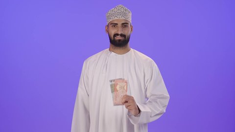 المساعدة والتبرع في شهر رمضان المبارك، بورتريه لرجل عماني عربي خليجي يرتدي الزي التقليدي يحمل بيده مجموعه من النقود الورقية، العبادة والتقرب الى الله ، اخراج زكاة المال للمحتاجين ، جمعيات خيرية في السعودية ، خلفية بنفسجية