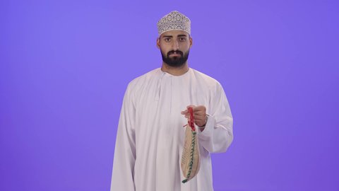 العبادة والتقرب الى الله، بورتريه لرجل عربي خليجي عماني يرتدي الدشداشة و الكمه يقوم بتقديم كيس الارز ، اخراج زكاة الفطر من الارز للمحتاجين ، زكاة الزروع والحبوب ، مفهوم العطاء والصدقة ، منتج محلي وطني